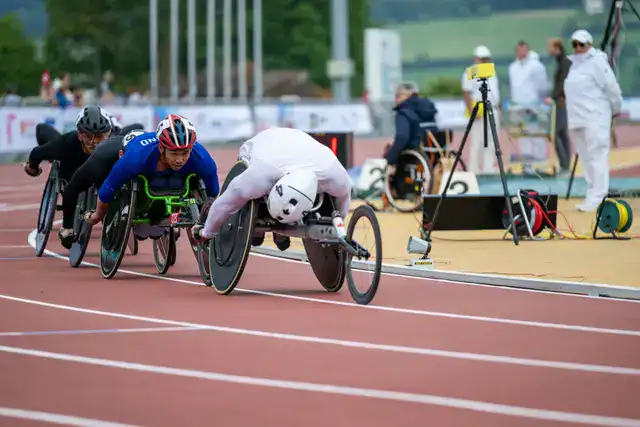 Wheelchair athletes competing in a sprint race on a track.