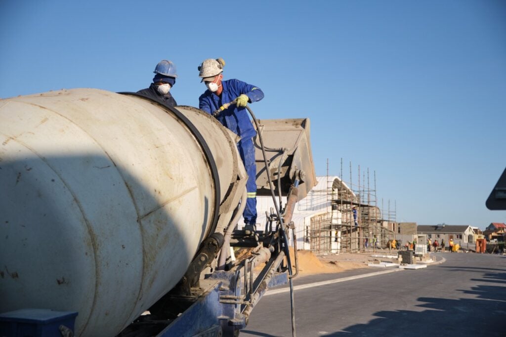 Construction workers operating a concrete mixer truck at a building site in South Africa.