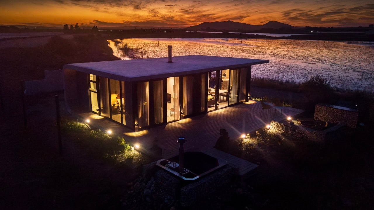 Design Philosophy Modern lakeside house illuminated at sunset with scenic water views in South Africa.