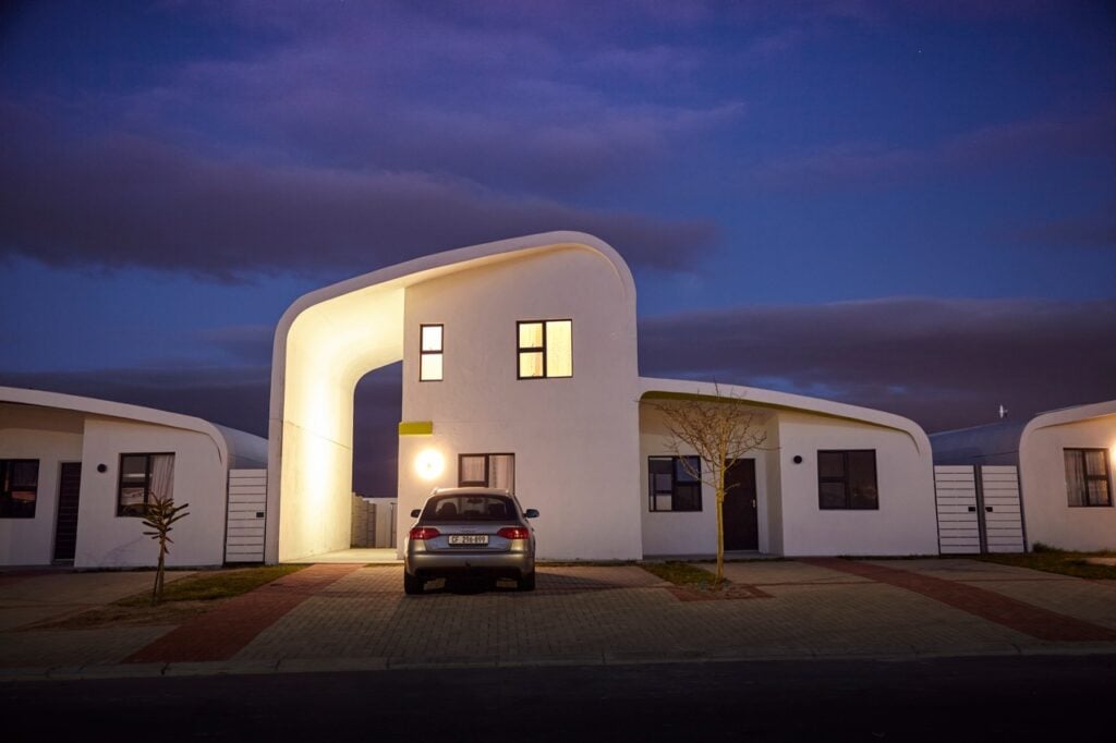 Modern white residential building with unique curved architecture at dusk, illuminated windows, and.