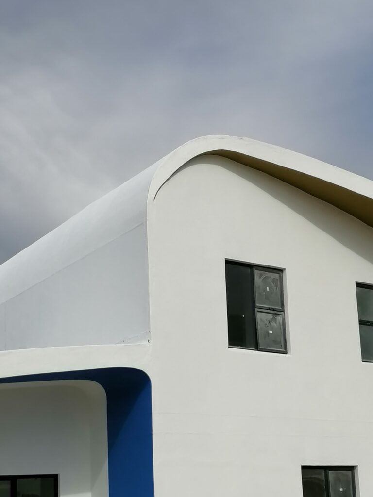 Modern white building with curved architectural design and large windows, showcasing innovative cons.