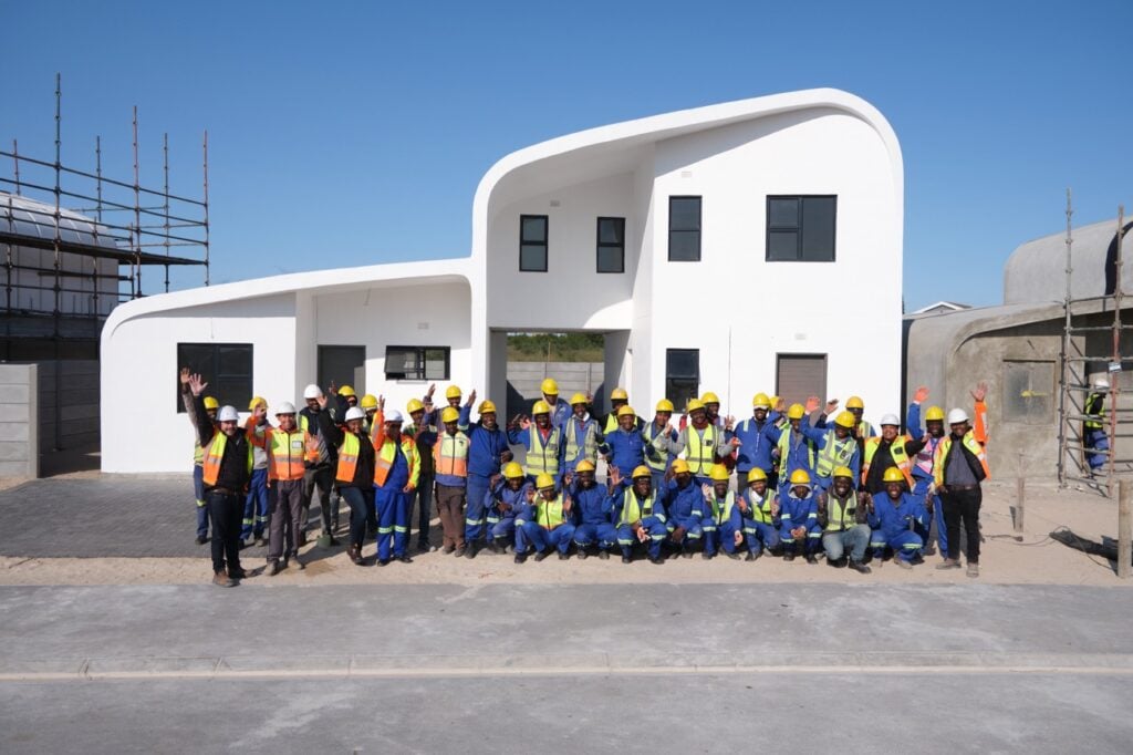 Construction workers and engineers posing in front of a modern, white residential building under con.