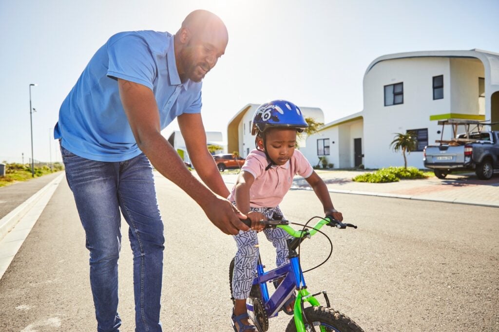 Man teaching girl to ride a bicycle outdoors in a modern residential area.