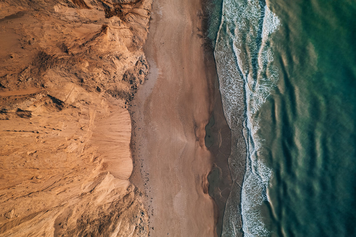 Coastal cliff with sandy beach and ocean waves in a scenic landscape.