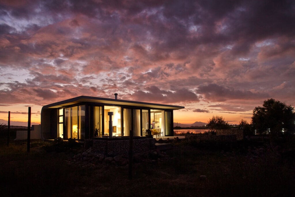 Contemporary glass house illuminated at dusk, showcasing sleek architecture and scenic surroundings.