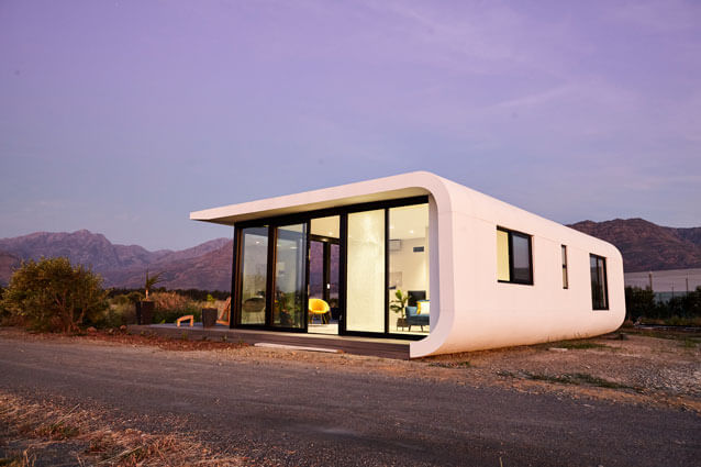 Modern minimalist tiny house with curved design and large glass windows in a desert landscape.
