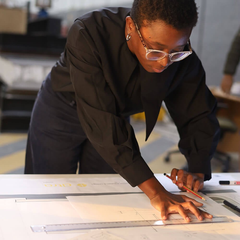 An architect leaning over a drafting table using a ruler and pencil to work on architectural blueprints.