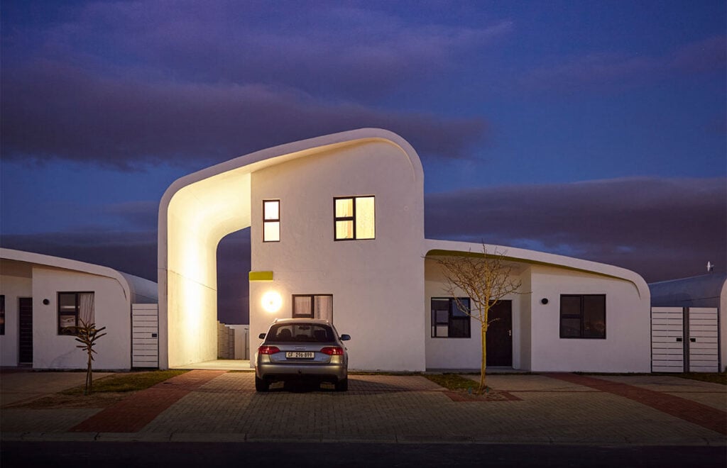 Modern white residential building with curved architectural design at dusk, illuminated windows and.