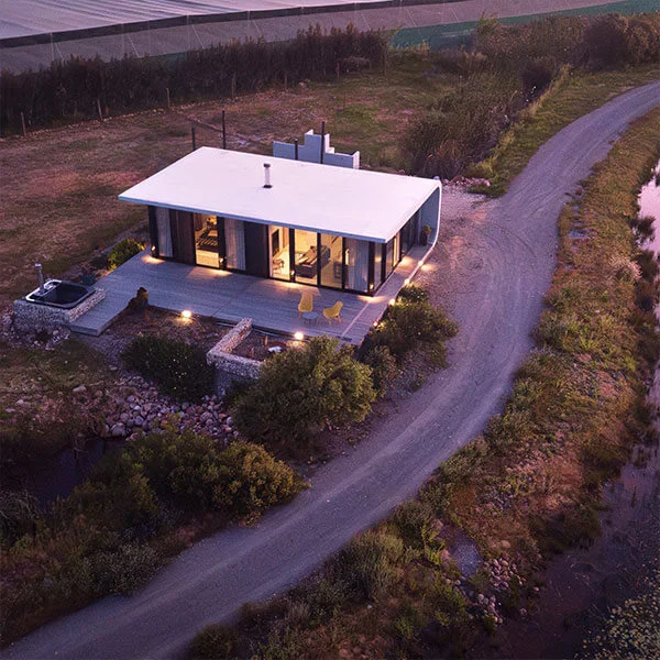Contemporary minimalist house with large glass windows, situated in a rural landscape with lush gree.