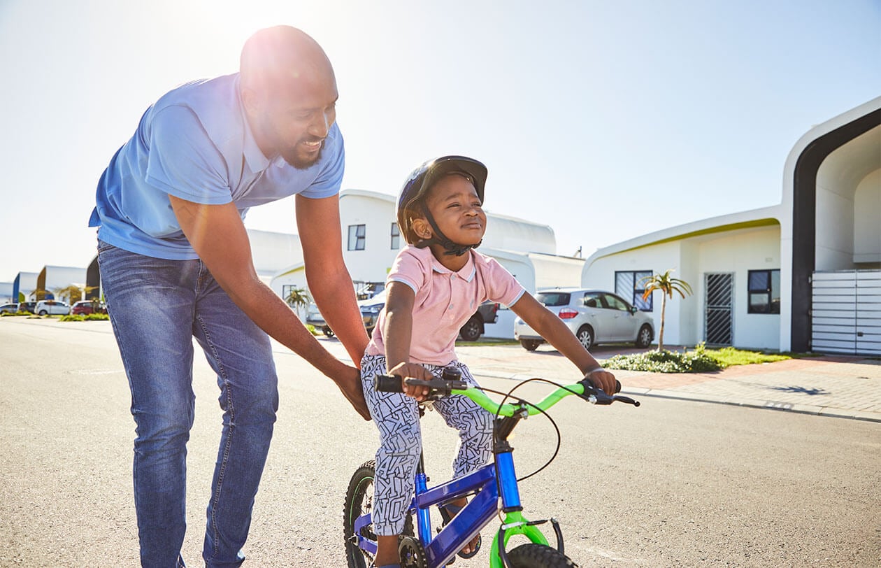 Social Impact Father helping daughter learn to ride a bike outdoors.