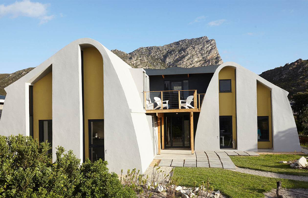 Design Philosophy Unique modern mountain house with curved white walls and large windows in a scenic landscape.
