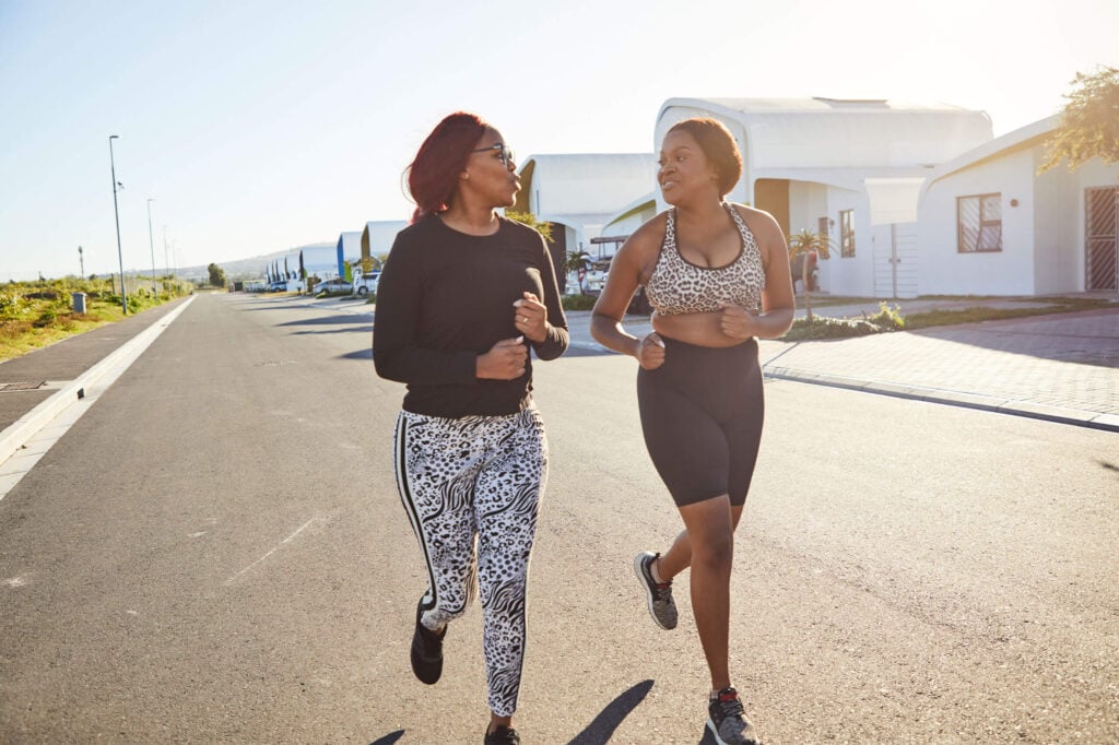 Running women exercising outdoors in a residential area, promoting health and fitness.