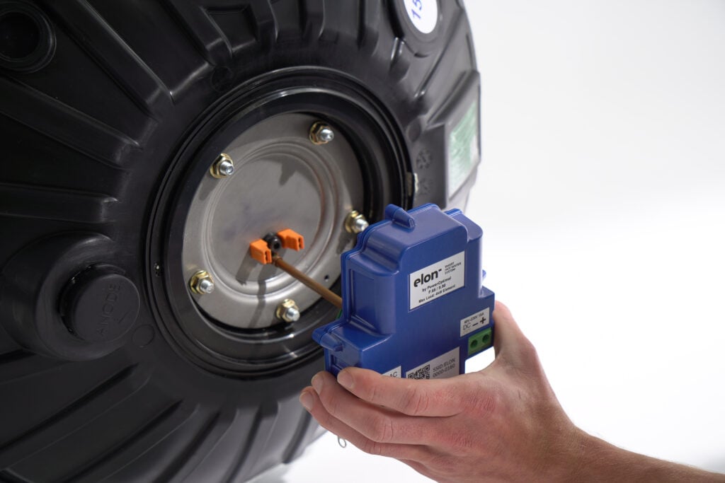 A hand connecting a blue Elon Smart Hot Water System controller module to the heating element flange of a black hot water tank.